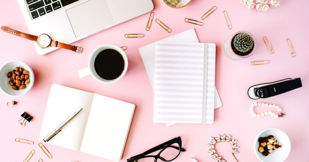 Flat lay of scattered new job gift ideas on a pink desk
